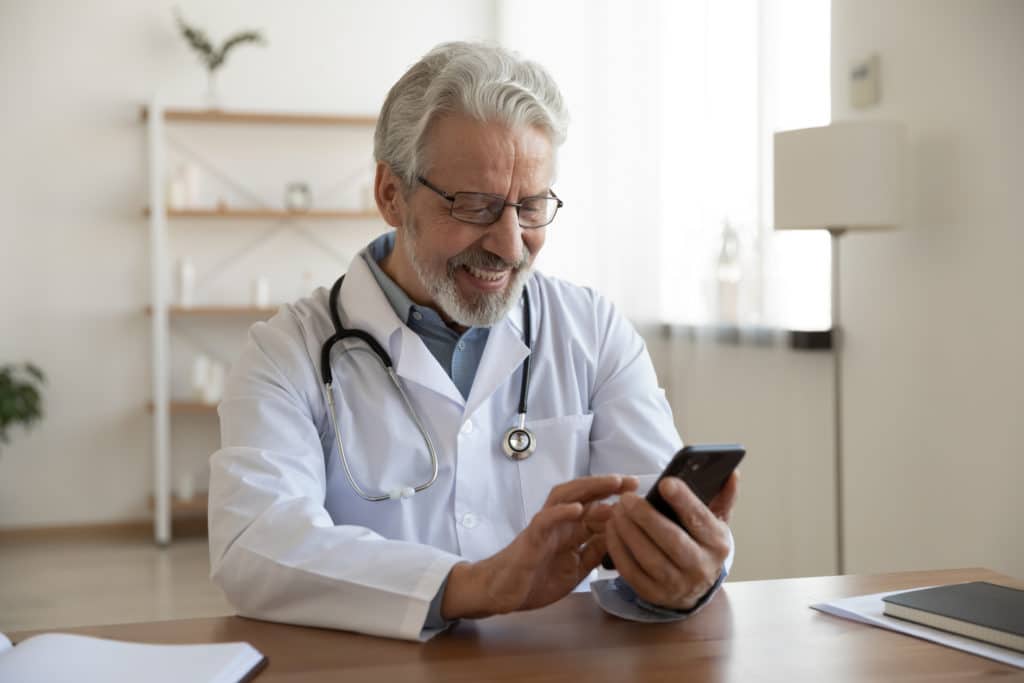 A doctor smiling while using a phone, taking care to avoid HIPAA Violations
