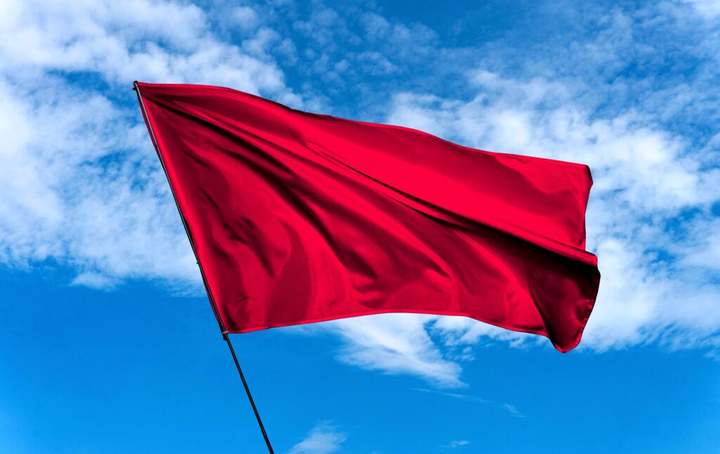 large red flag agains a bright blue sky with wispy clouds