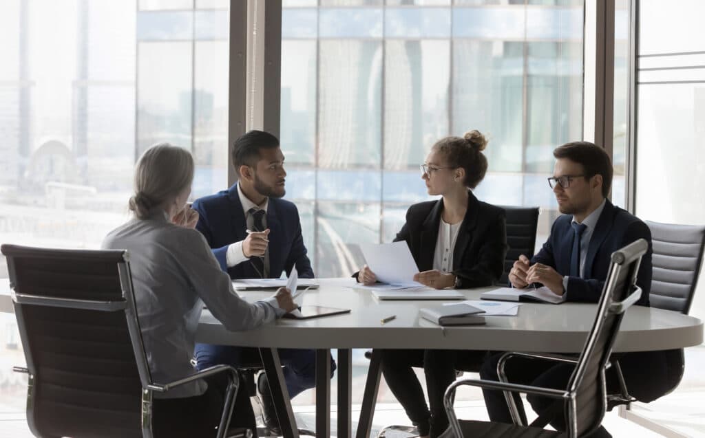 Four professionals in business attire sit around a conference table in a modern office, engaged in a discussion about how personal injury firms can invest smarter to thrive in a high-competition market, with documents and laptops spread before them.